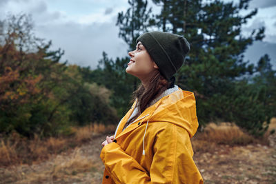 Side view of young woman standing against trees