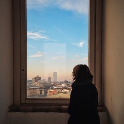 Rear view of woman looking at view of cityscape through winow