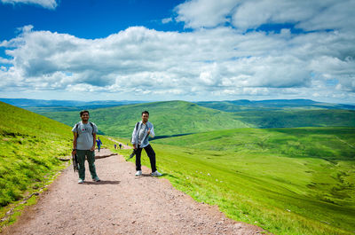 Rear view of men walking on mountain against sky