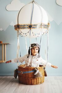 Portrait of boy sitting wicker basket against wall