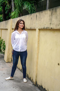 Portrait of young woman standing against wall