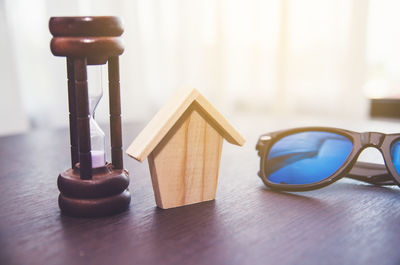 Wooden model house with hourglass and sunglasses on table