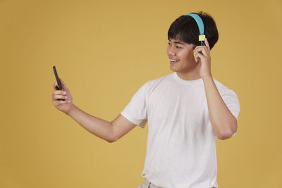 Young woman using mobile phone against yellow background