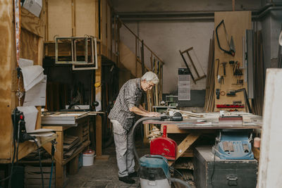 Side view of senior male carpenter working on laptop while standing at repair shop