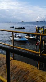 Boats moored by pier at sea against cloudy sky