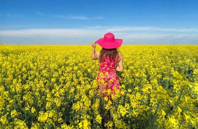 Rear view of woman standing in canola field during sunny day