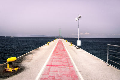 Empty road leading towards sea against clear sky