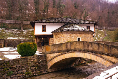 Arch bridge amidst trees and building in forest