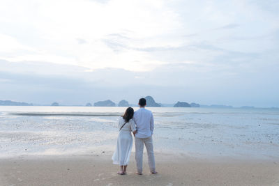 Rear view of couple on beach against sky