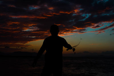 Silhouette man standing by sea against sky during sunset