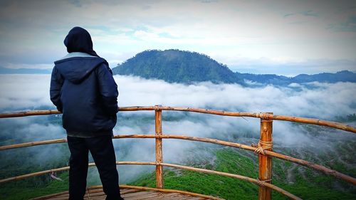 Rear view of man standing on railing against mountain