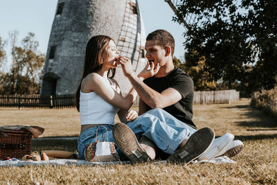 A young couple feeds grapes to each other on a picnic in the park.