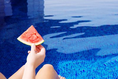 Low section of woman holding strawberry against swimming pool