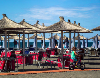 Side view of boy riding bicycle against parasols at beach