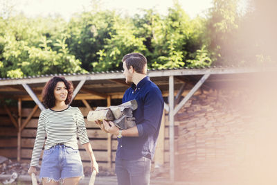Man and woman talking while carrying firewood against shed