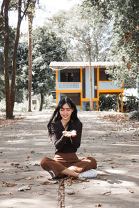 Full length portrait of woman sitting against trees