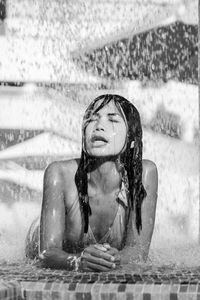 Water spraying on young woman while lying in fountain