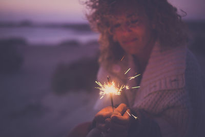 Woman holding illuminated sparkler at beach during sunset