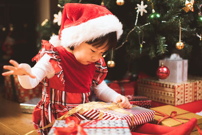 Girl opening gift while siting by christmas tree