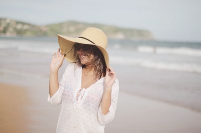 Cheerful woman wearing hat while standing at beach
