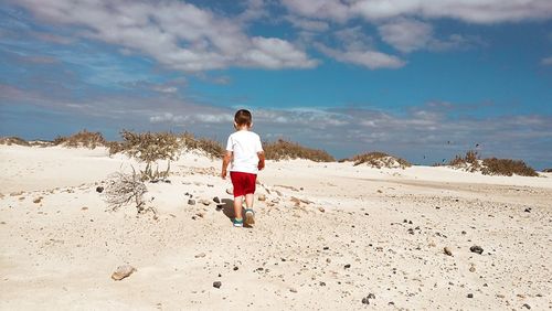 Rear view of boy walking on beach against sky