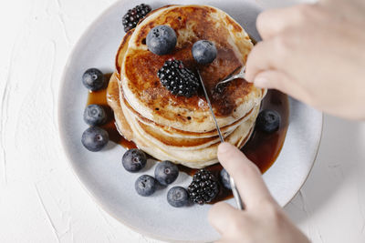 Woman about to cut a slice of a stack of pancakes with berries and syrup