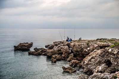 People on rock by sea against sky