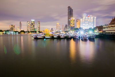 River by illuminated city buildings against sky
