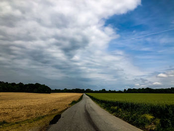 Empty road amidst field against sky