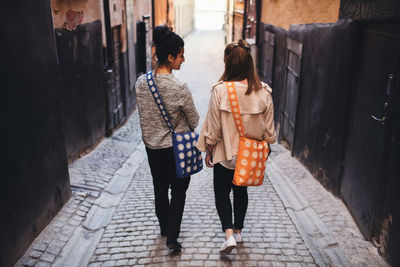 Rear view of friends talking while walking on alley amidst buildings in town