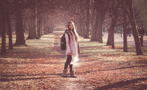 Full length of woman standing by tree trunk during autumn