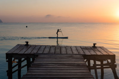 Side view of silhouette of unrecognizable female surfing on paddledboard on calm sea water at sunset in summer