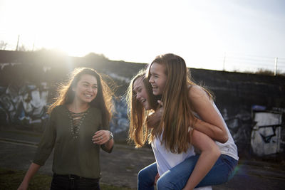 Teenage girl looking at friends piggybacking during sunny day