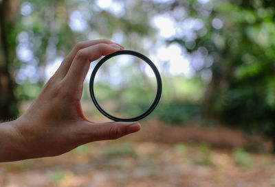 Close-up of hand holding bangle against blurred trees
