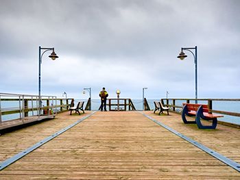 Man on long touristic mole within autumn misty morning. tourist at handrail. wet wooden board