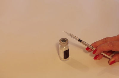 Close-up of hand holding injection on white table