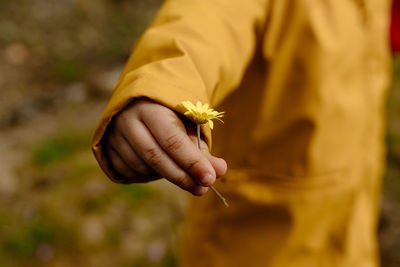 Cute child with yellow jacket holding yellow flower