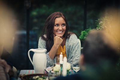 Smiling young woman sitting at dining table during party in back yard
