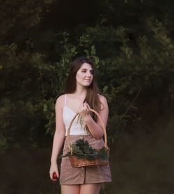 Woman holding basket while standing against trees