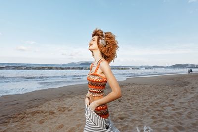 Rear view of woman standing at beach against sky