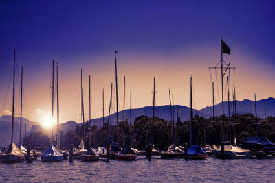 Sailboats moored on shore against sky during sunset