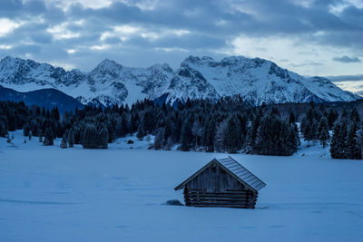 House on snowcapped landscape against cloudy sky