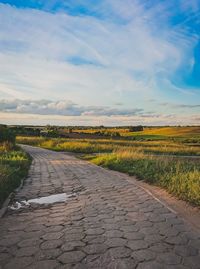 Empty road amidst field against sky