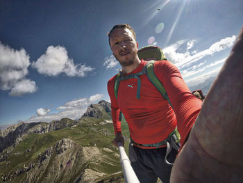 Portrait of hiker holding selfie stick on mountain against sky
