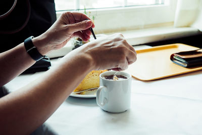 Cropped hands of person having food and drink at table by window