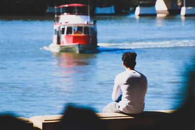 Rear view of man sitting on jetty by sea