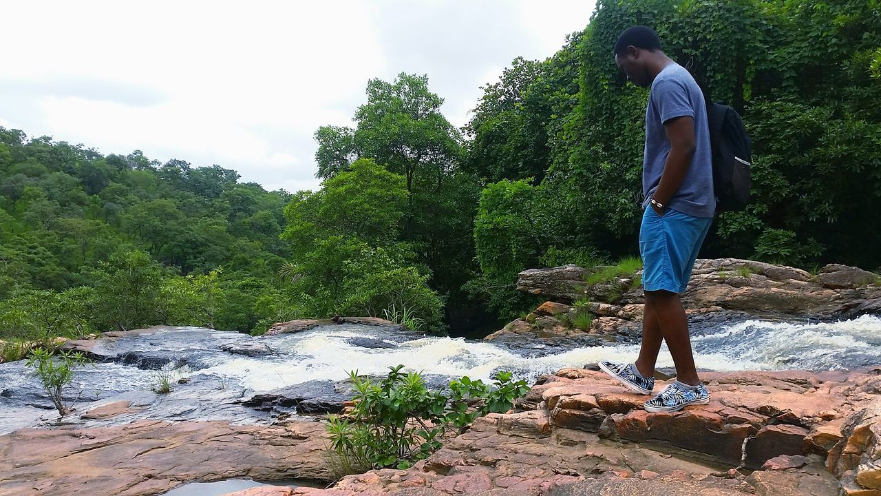 lifestyles, leisure activity, standing, tree, full length, casual clothing, rear view, men, nature, sky, rock - object, tranquility, growth, beauty in nature, day, forest, low section, mountain