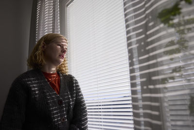 Pensive teenage girl looking through window