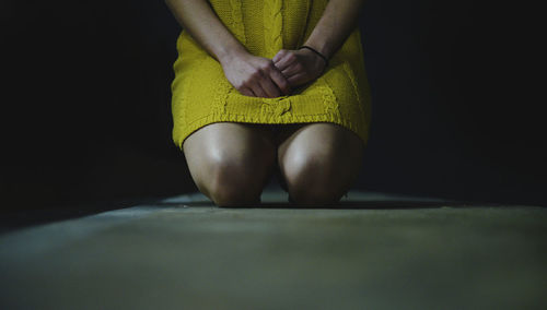 Midsection of woman praying while kneeling on floor