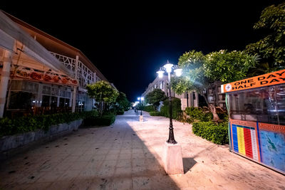 Illuminated street amidst buildings against sky at night